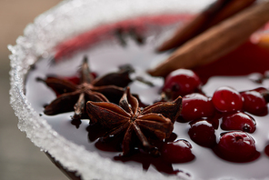 close up view of red spiced mulled wine with berries, anise, orange slices and cinnamon in glass decorated with sugar