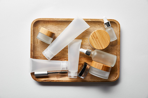 top view of different cosmetic containers on wooden tray on white