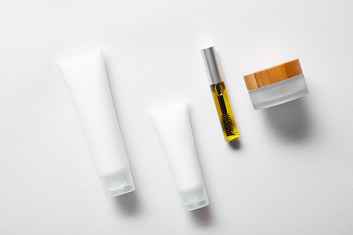 top view of cream tubes with hand cream, empty jar and mascara bottle with oil on white