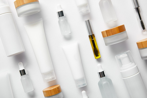 flat lay of cream tubes with hand cream, mascara bottles, cosmetic glass bottles, cosmetic dispensers and jars on white