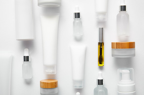 flat lay of cream tubes with hand cream, mascara bottle with oil, cosmetic glass bottles, cosmetic dispensers and jars on white
