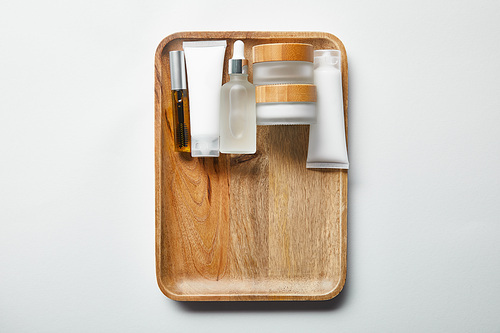various cosmetic containers on wooden tray on white