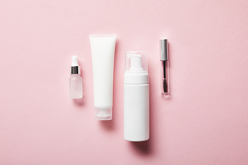 cream tube with hand cream, cosmetic dispenser, empty jar and mascara bottle on pink