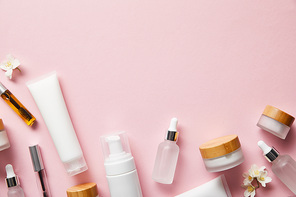 top view of cream tubes, cosmetic dispenser, empty jars and with hand cream, mascara bottles on pink