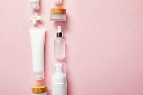 flat lay of different cosmetic containers and jasmine flower on pink