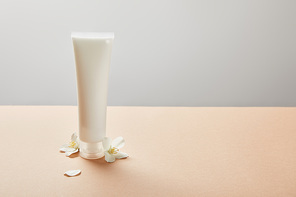 cream tube with cream and few jasmine flowers on beige isolated on grey