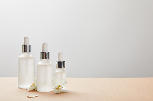 different sized cosmetic glass bottles and few jasmine flowers on beige