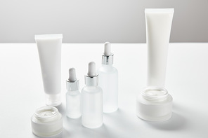 cream tubes, cosmetic glass bottles and open jars with cream on white