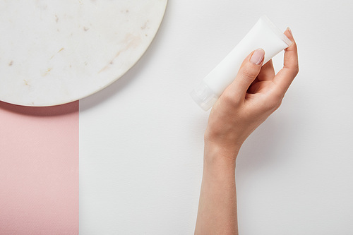 cropped view of woman holding cream tube near plate on white pink surface