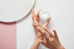 cropped view of woman holding cream in jar, applying cosmetic on skin