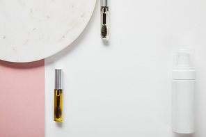 top view of mascara bottles and cosmetic dispenser near plate on white pink surface