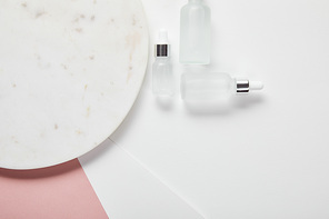 top view of cosmetic glass bottles near plate on white pink surface