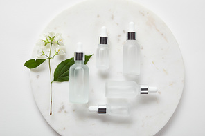top view of plate with jasmine and cosmetic glass bottles on white surface