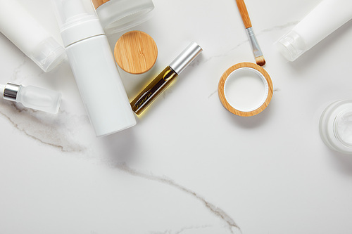 cropped view of cream tubes, cosmetics jars, dispenser and glass bottle with eye brush on white surface