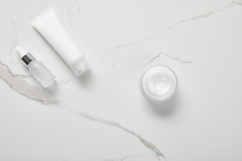 top view of cosmetic glass bottle, jar with cream and moisturizer tube on white surface