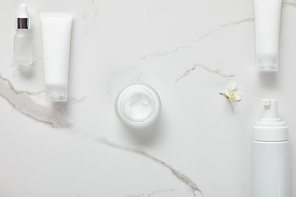 top view of cosmetic glass bottle, jar with cream, moisturizer tubes, dispenser and jasmine on white surface
