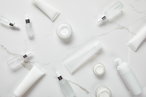 top view of cosmetic glass bottles, jars with cream, moisturizer tubes, dispenser and jasmine on white surface