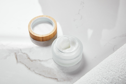 opened jar with cosmetic cream and wooden cap near towel on white surface