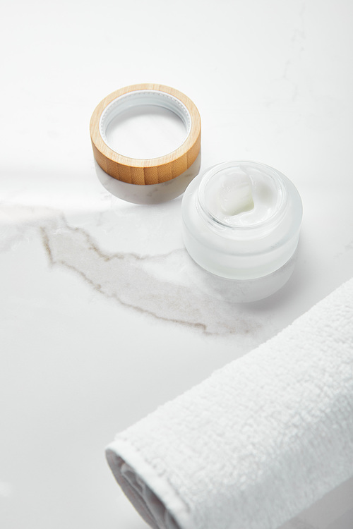 opened jar with cosmetic cream and wooden cap near towel on white surface
