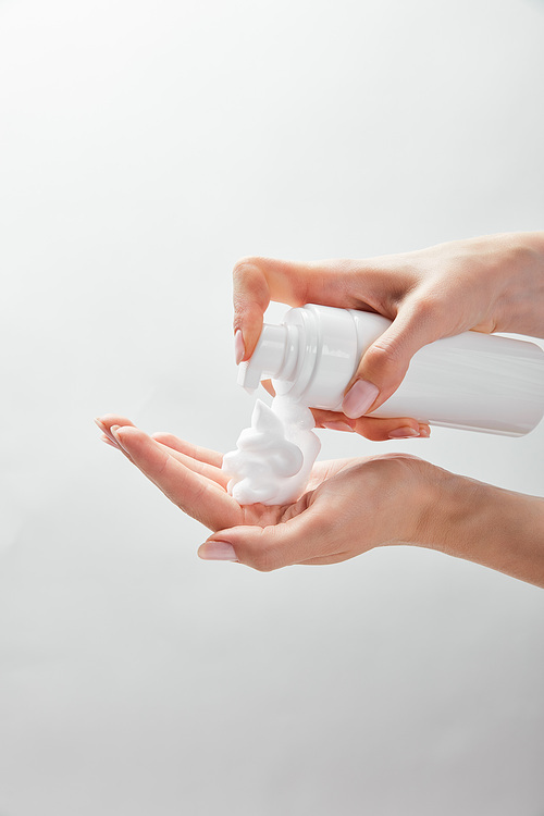 cropped view of woman using cosmetic dispenser with foam isolated on white