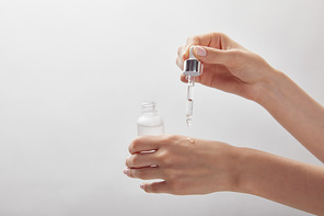 cropped view of woman holding cosmetic glass bottle, applying moisturizer serum on skin
