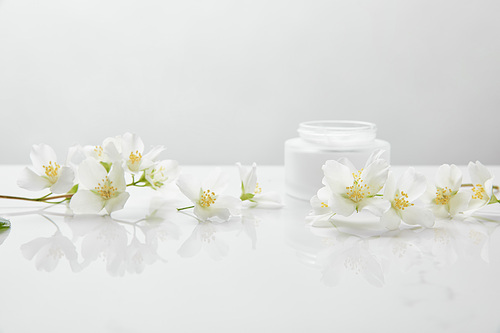jasmine flowers on white surface near jar with cream