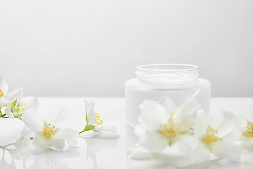 jasmine flowers on white surface near jar with cream