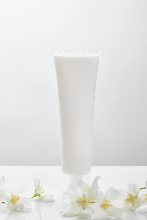 jasmine flowers on white surface near cosmetic cream in tube