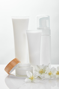 jasmine flowers on white surface near cream in tubes, jar and cosmetic dispenser