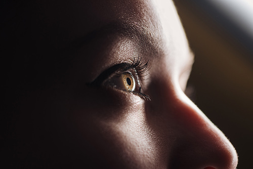 close up view of young woman eye with eyelashes and eyebrow looking away in dark