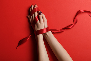partial view of woman tied with silk ribbon on red background
