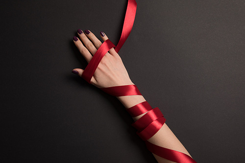 partial view of female hand with red ribbon on black background