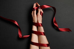 partial view of female hands in silk red ribbon on black background