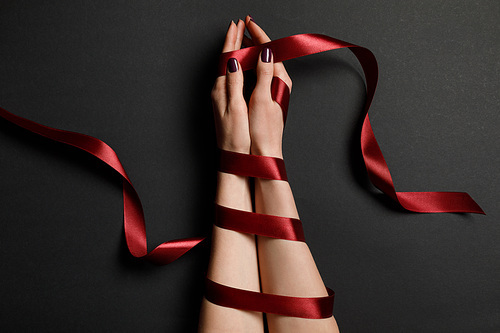 partial view of female hands in silk red ribbon on black background