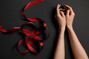 cropped view of female hands near satin red ribbon on black background