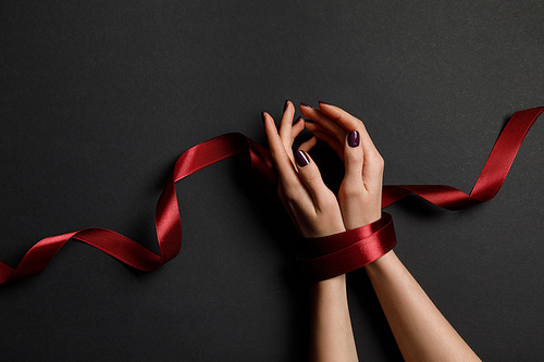 cropped view of woman tied with silk red ribbon on black background