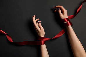 partial view of female hands in red ribbon on black background