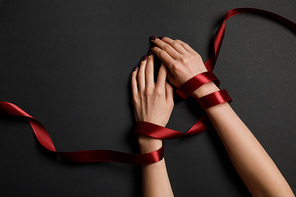 partial view of female hands in satin red ribbon on black background