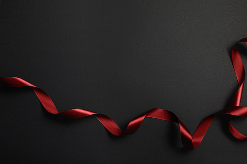 top view of red silk wavy ribbon on black background with copy space