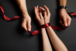 cropped view of man tying red satin ribbon on female hands