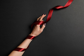 cropped view of female hand and satin red ribbon on black background