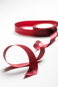 selective focus of silk wavy burgundy ribbon with spool on grey background