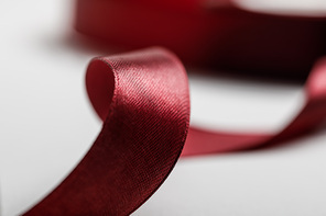 selective focus of shiny silk curved burgundy ribbon on grey background