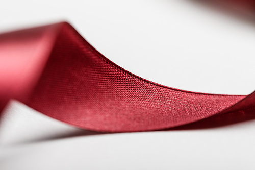 close up of shiny silk curved burgundy ribbon on grey background