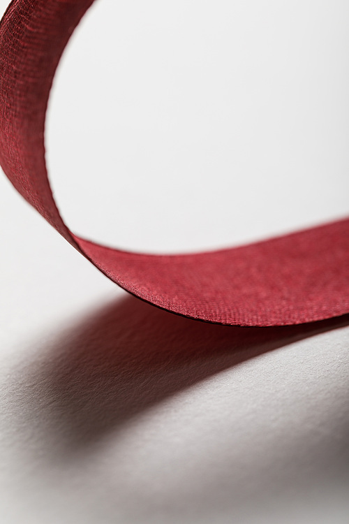 close up of shiny silk wavy burgundy ribbon on grey background