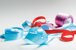 curved blue, red and purple satin ribbons with spools on grey background