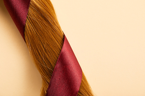 Top view of burgundy ribbon on brown hair on beige background