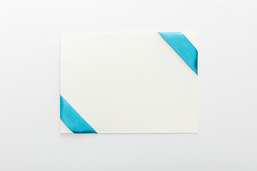 top view of blank card with blue decorative satin ribbon on white background