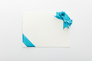 top view of blank card with blue decorative satin ribbon and bow on white background
