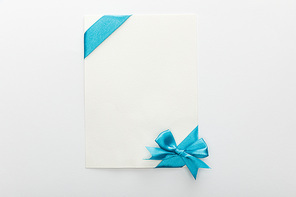 top view of blank card with blue decorative satin ribbon and bow on white background